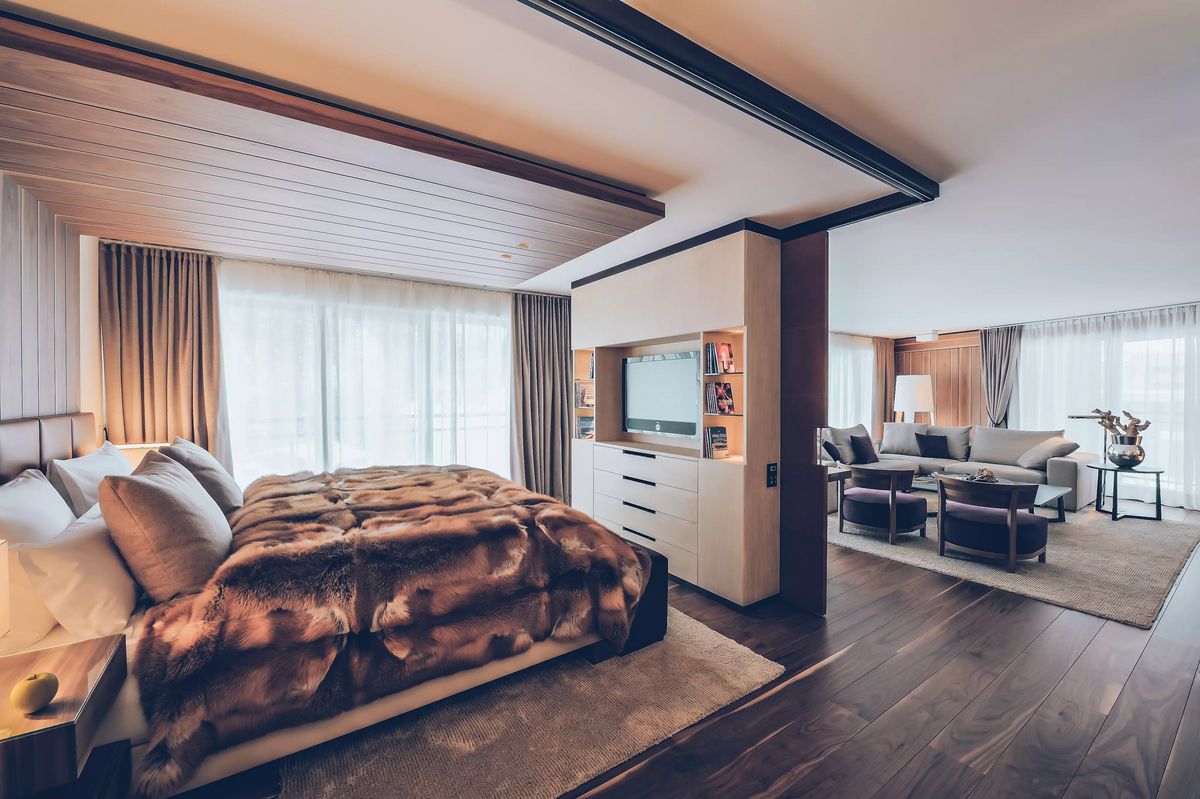 Luxuriöse Suite mit Fellbettdecke, Wohnbereich mit Sofa, Sessel und großer Fensterfront